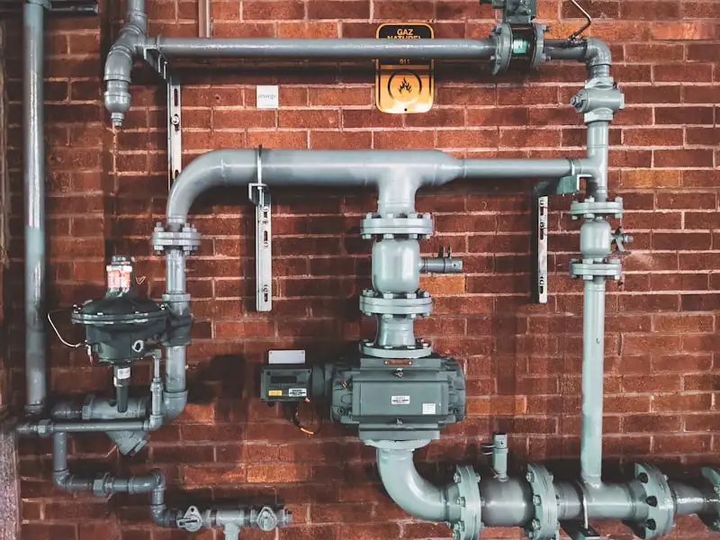 Industrial pipework, valves, and a pump mounted on a brick wall